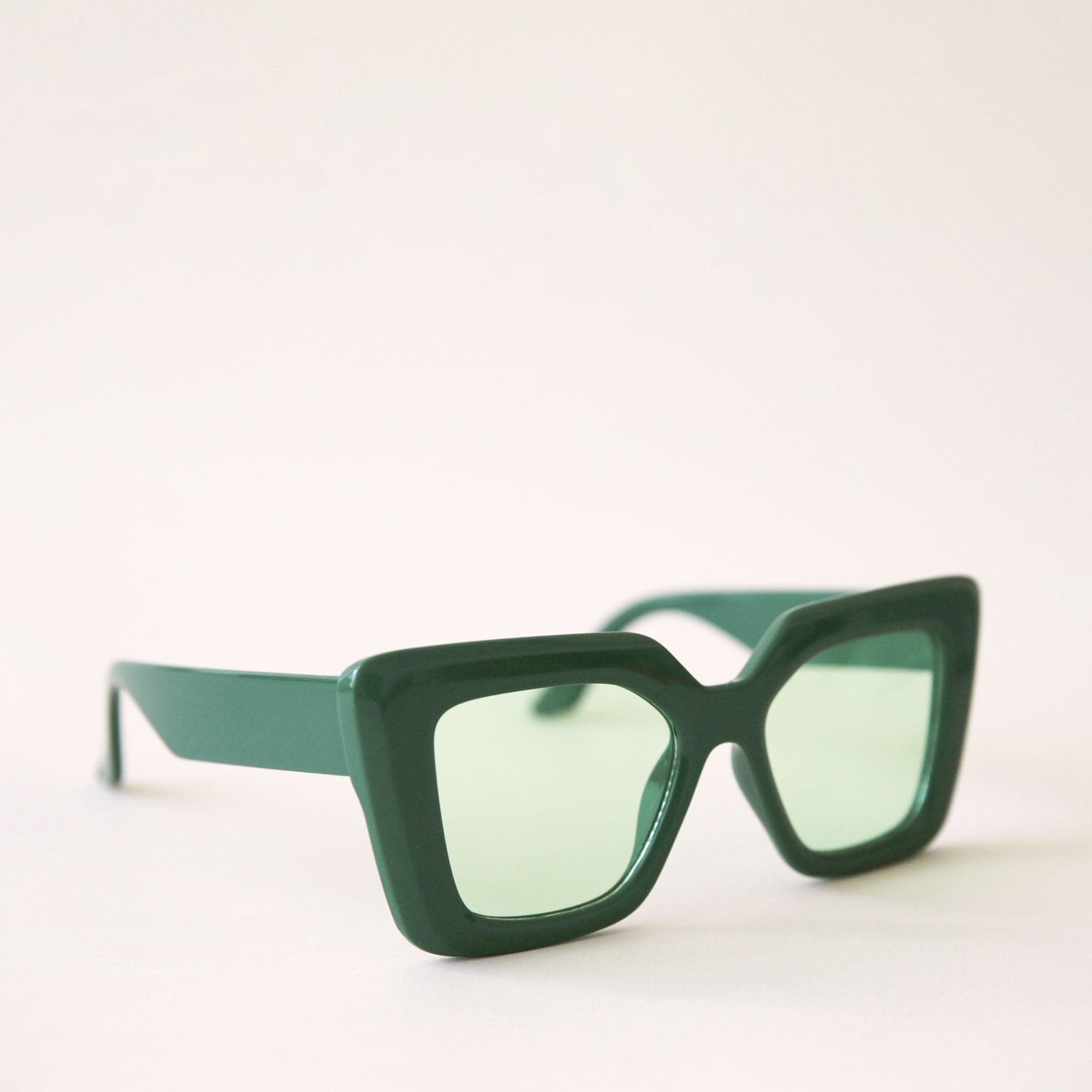 70's inspired sunglasses with a dark green, rectangle frame that has a slight cat eye point at the tops along with light green lenses.