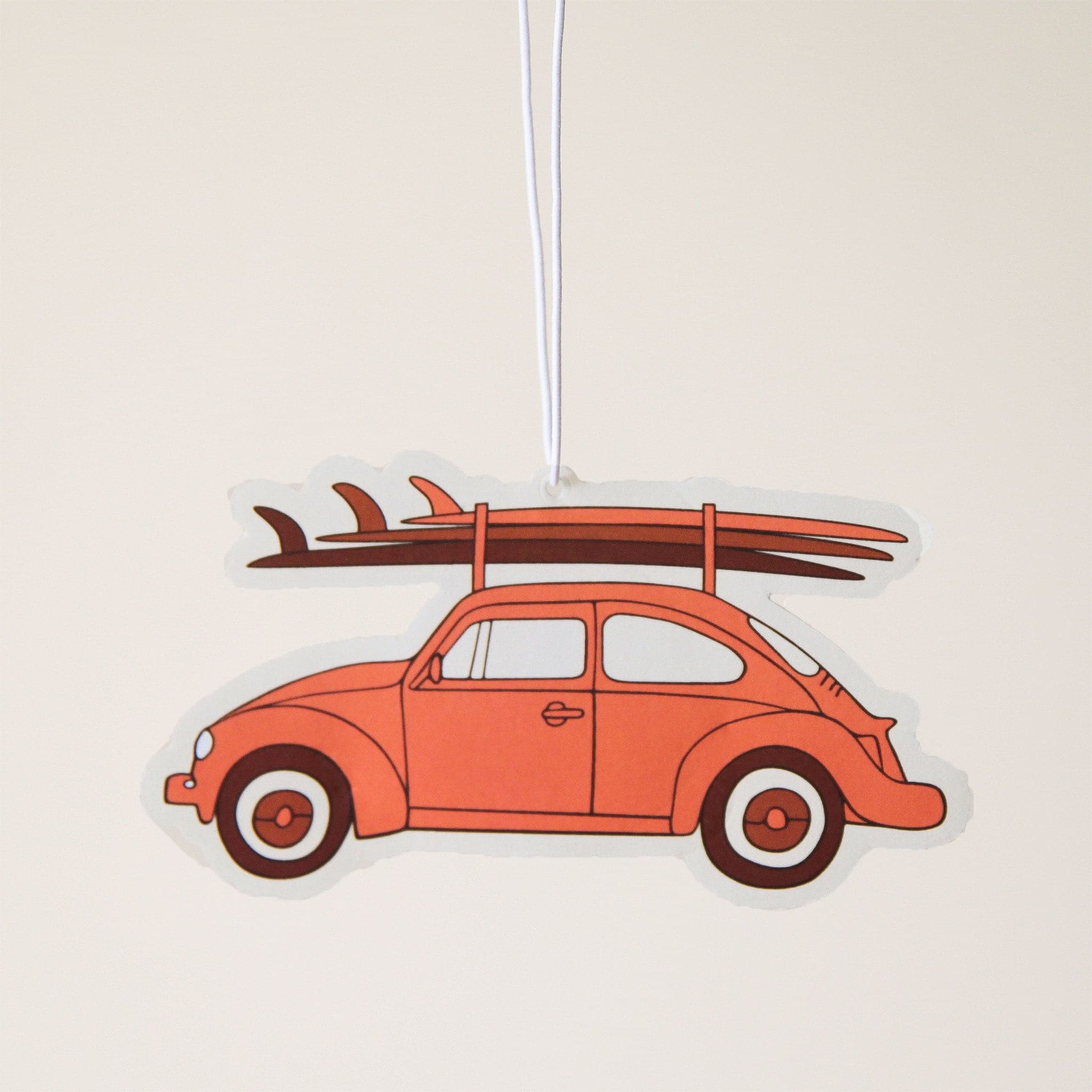 An air freshener in the shape of a brownish red VW bug with 3 surf boards on the roof.