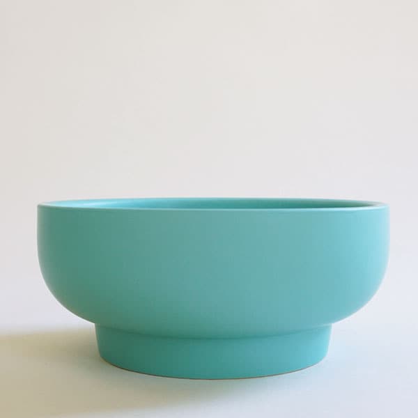 In front of a white background is a bright blue pedestal bowl. The bowl is wide with a short pedestal bottom. 