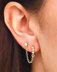 On a model's ear is a stud earring with a chain connecting to another stud earring. 