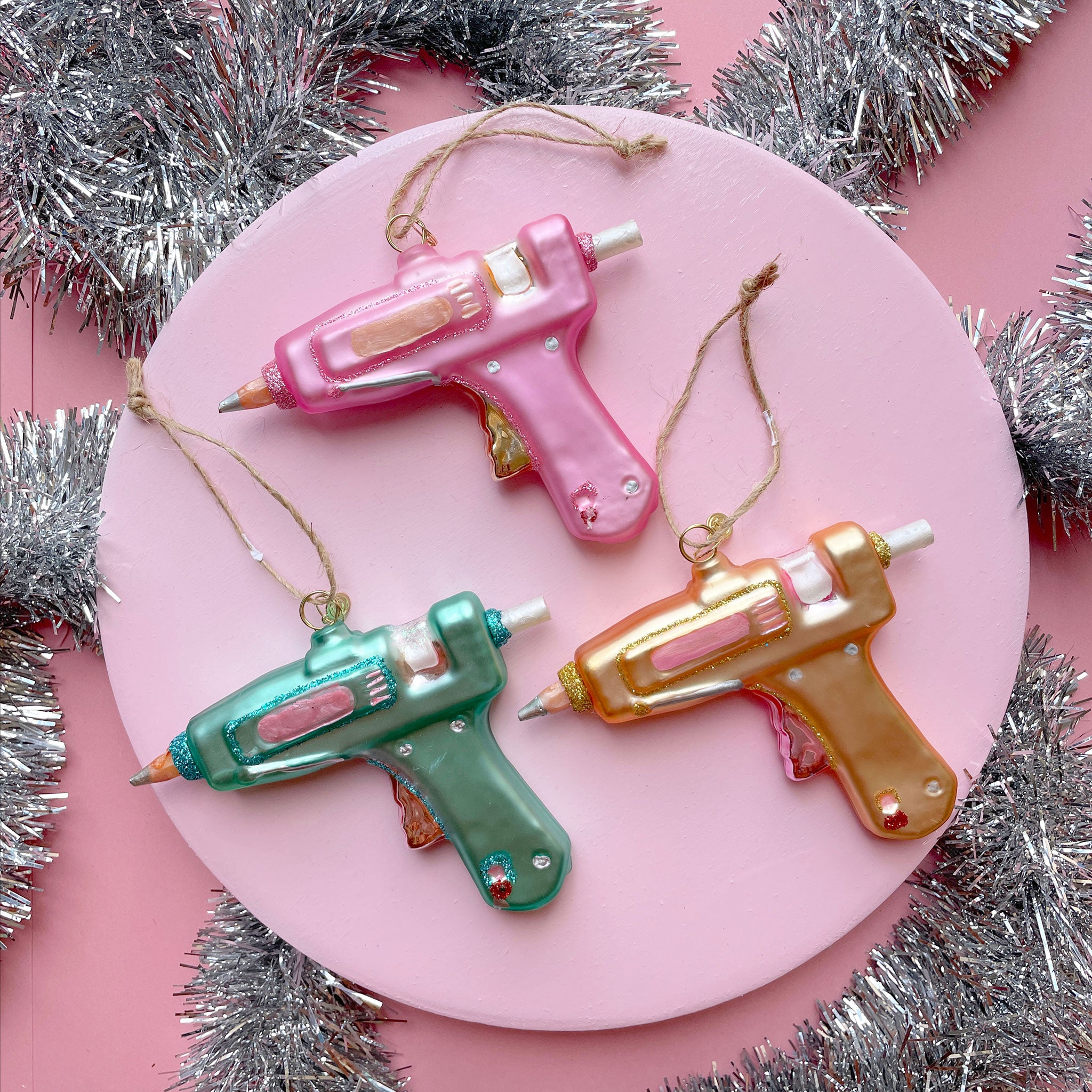 Hot Pink, Blue, and Yellow glass hot glue gun ornaments surrounded by silver tinsel.