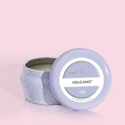 A small lavender tin candle with white wax and a white diamond repeating pattern on the outside of the tin. Comes with a matching purple lid that reads, "Capri Blue Volcano".