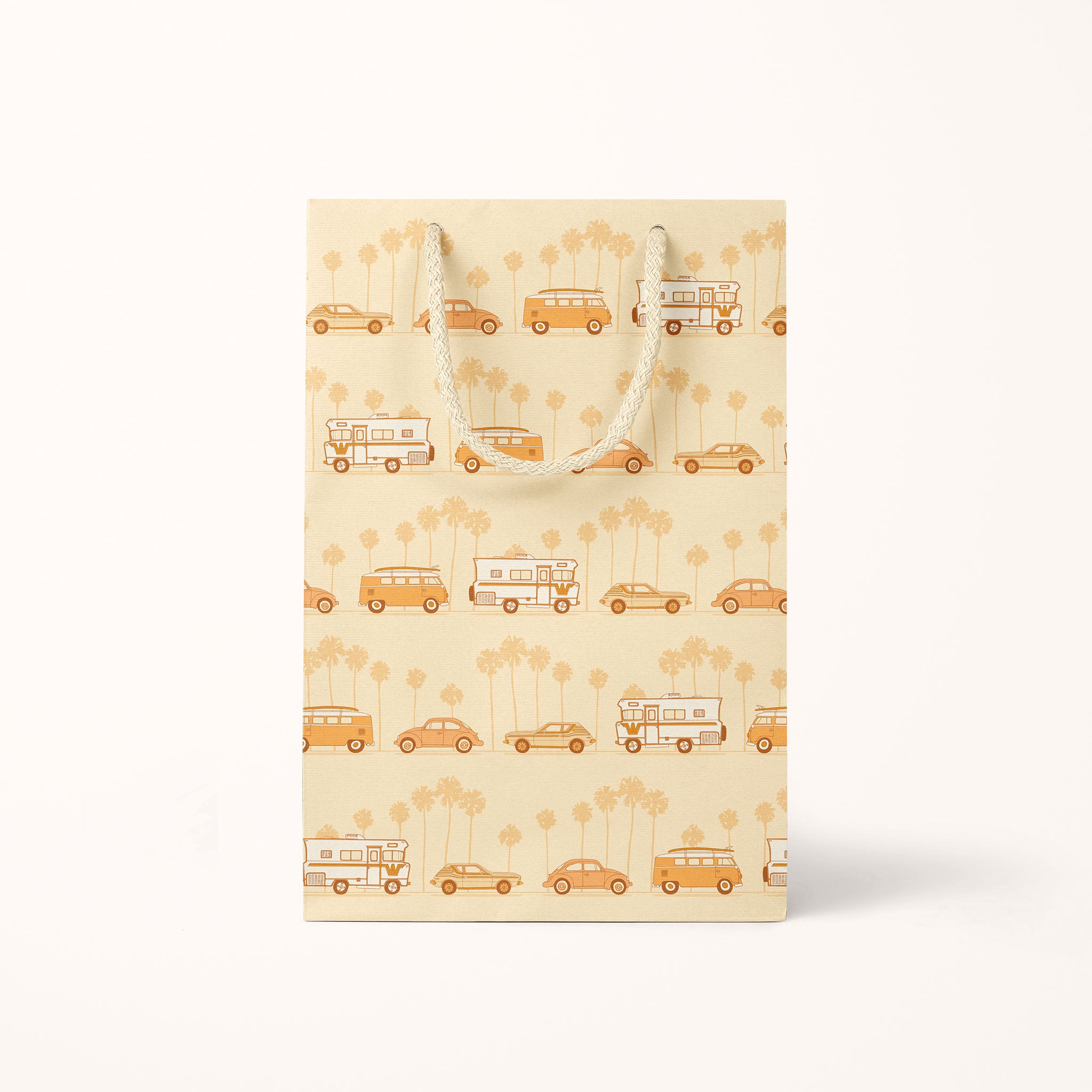 An orange paper gift bag with a VW van with a surfboard on top in front of faded palm trees and text that reads, "Cowabunga Christmas". The smaller bag has a repeating print with a vintage VW bus, camper and bug.