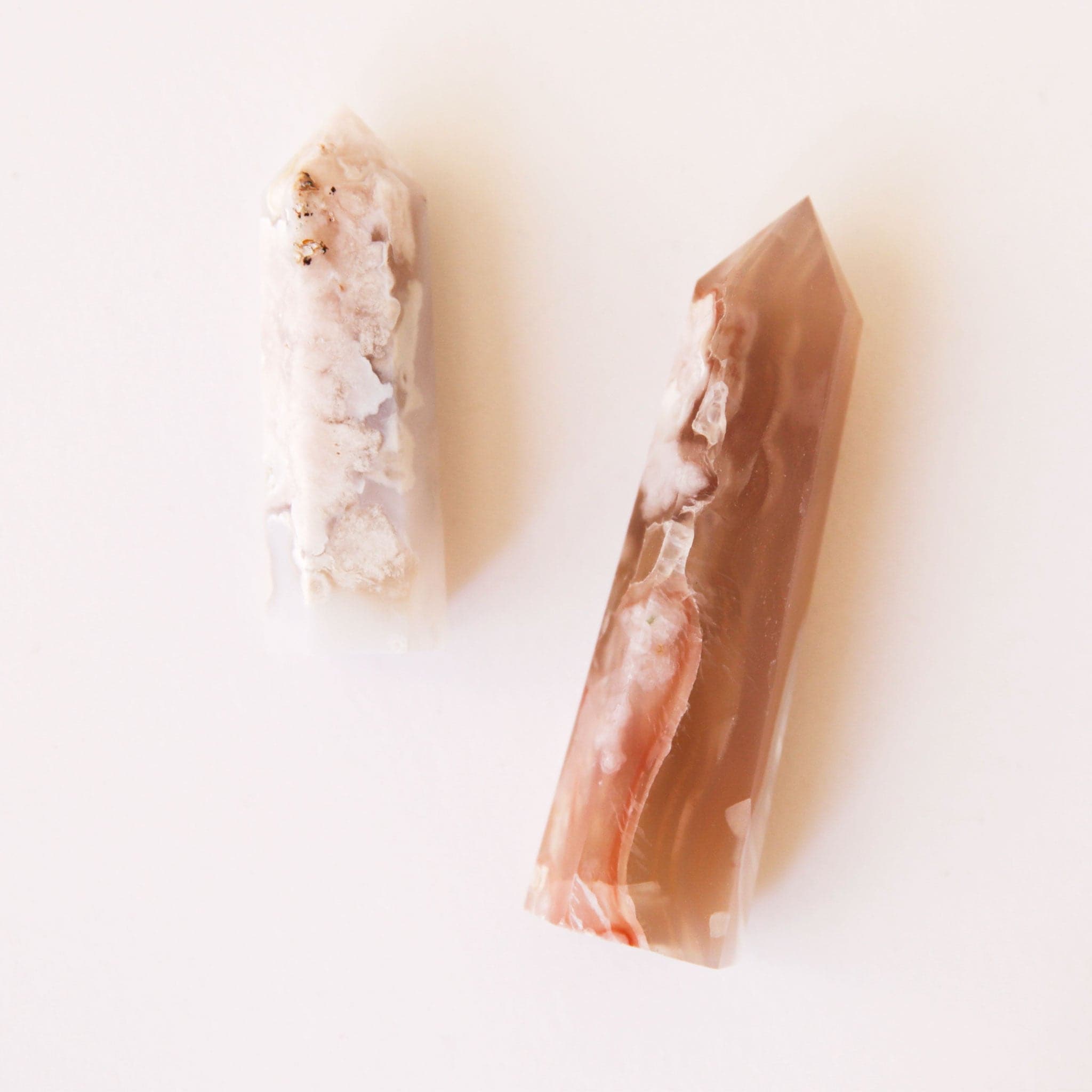 A photo of two cherry blossom crystals, rose pink, creams and burnt reds in color. The two sizes represent the two sizes available for purchase. Each crystal is sold separately. These cherry blossom agate crystals are in the shape of a point and are flat on the bottom to allow them to be freestanding.