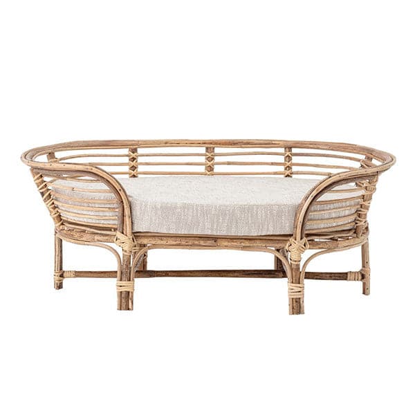 In front of a white background is a rattan dog bed. The dog bed is an oval shape with six rattan legs on the bottom. Inside the bed is a light gray bed cushion. 