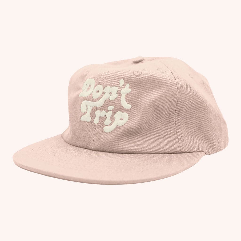 A light pink 6 panel hat with a flat brim and the phrase, " Don't Trip" in white embroidering.