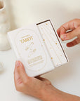 A cream box of 78 Tarot cards with an illustration of two hands and a star in between. All cards are beautifully illustrated with descriptions underneath and detailed with gold foiling.