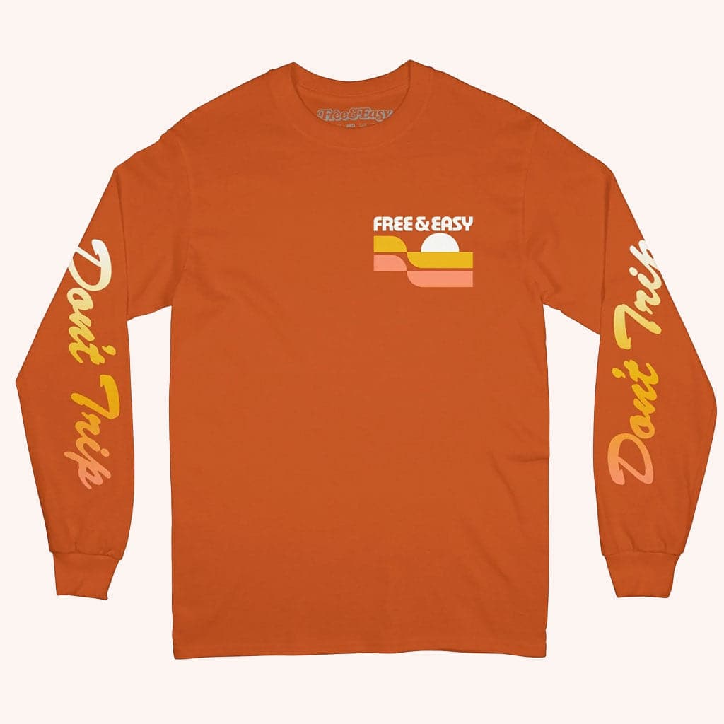 The front of this orange long-sleeved t-shirt has "Don't Trip" in yellow does the arms and a small graphic that says "Free & Easy" in he top left corner of the shirt.