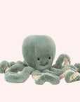 In front of a white background is a light blue stuffed octopus. On his head are two black eyes and a small black mouth. The bottom of his tentacles is cream colored. 