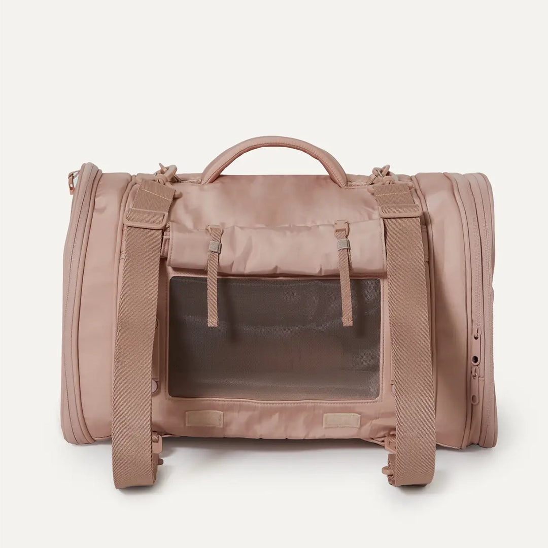 A nude colored pet carrier with an outside pocket for storing essentials and a zipper opening on both ends along with a handle on the top and two attachments for a shoulder strap option. There is a mesh opening on the side of the carrier that can also be covered with a folded flap.