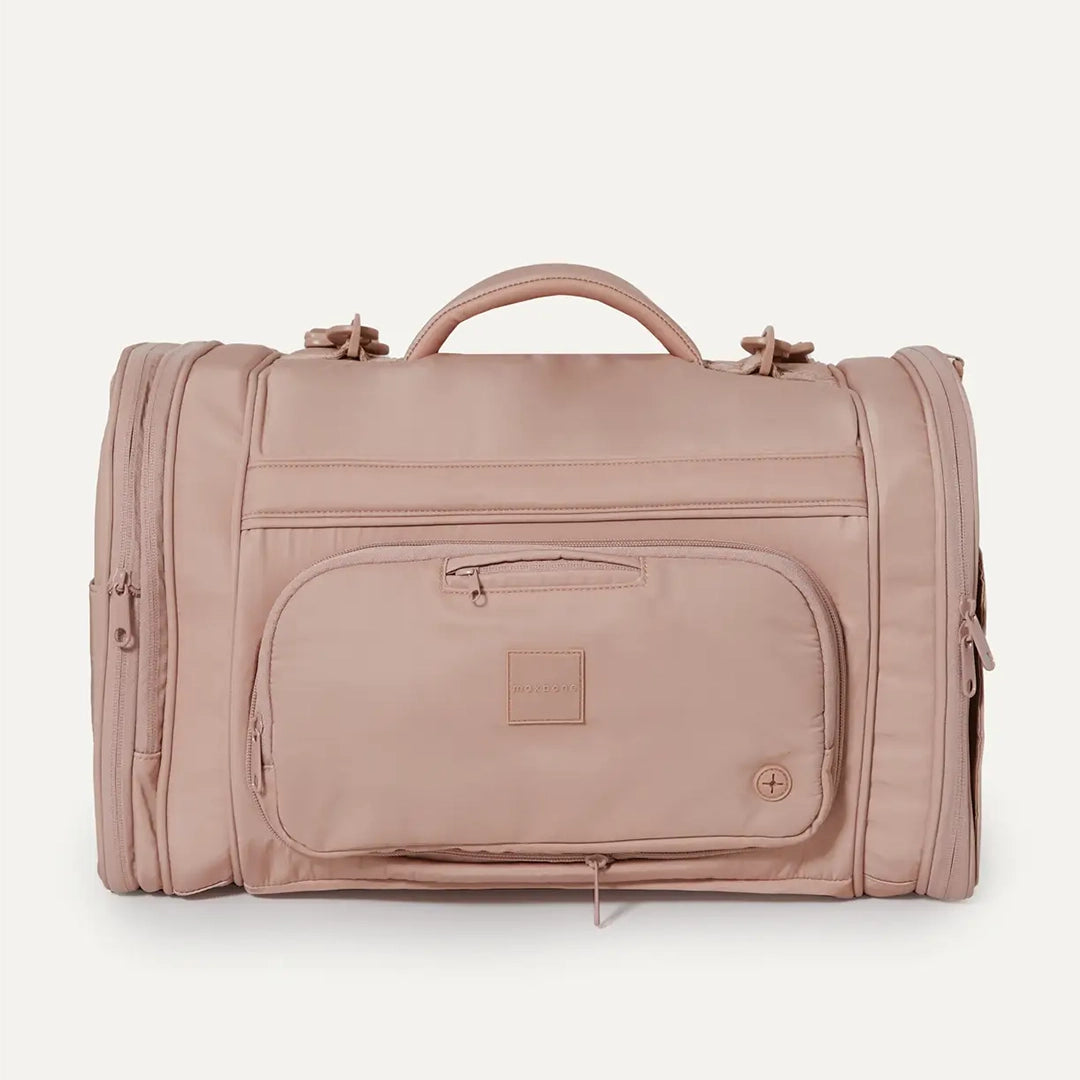 A nude colored pet carrier with an outside pocket for storing essentials and a zipper opening on both ends along with a handle on the top and two attachments for a shoulder strap option.