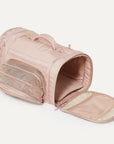 A nude colored pet carrier with an outside pocket for storing essentials and a zipper opening on both ends along with a handle on the top and two attachments for a shoulder strap option. There is a mesh opening on the side of the carrier that can also be covered with a folded flap.