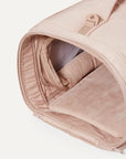 A nude colored pet carrier with an outside pocket for storing essentials and a zipper opening on both ends along with a handle on the top and two attachments for a shoulder strap option. There is a mesh opening on the side of the carrier that can also be covered with a folded flap.