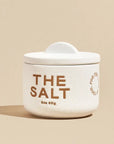 A 3oz bespoke pinch pot with a half moon lid that marries form and function along with brown text on the front that reads, "The Salt 3oz 85g".