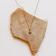 A gold chain necklace with a tiny eight pointed star charm along with a single CZ stone in the center.