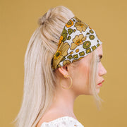 A satin cream headband with an orange, muted yellow, and olive green floral pattern photographed here being worn on a model with a half up half down hairstyle.