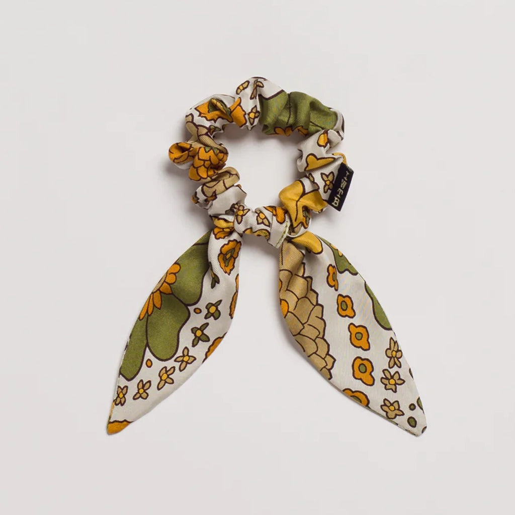 A satin scrunchie hair tie that has a yellow, olive green and white floral pattern on it.